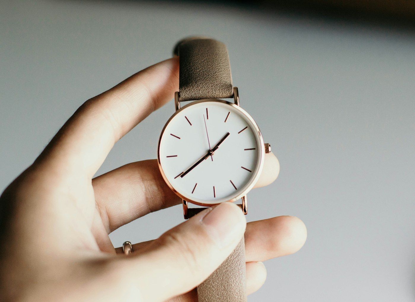 A classic round dress watch with a white dial and tan leather strap, held in one hand.