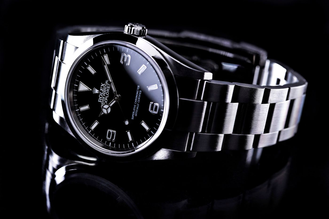 A steel sports watch with a black dial photographed under dramatic lighting.