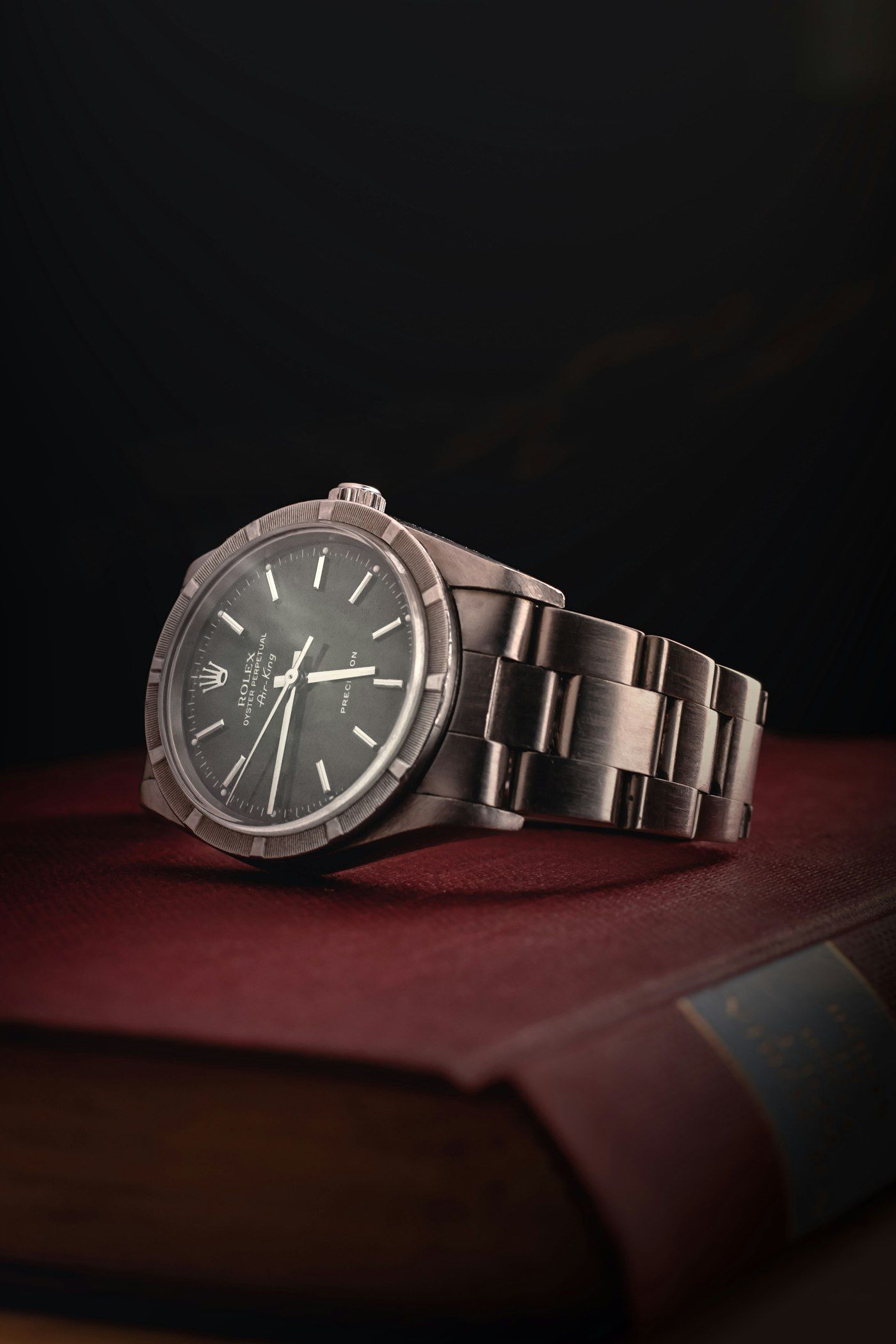 A vintage-style steel automatic watch with a dark dial on a deep red surface.